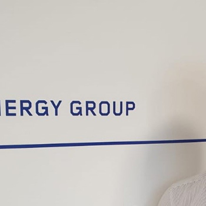 A man in a white shirt stands next to a wall displaying the text "The 3T Energy Group.