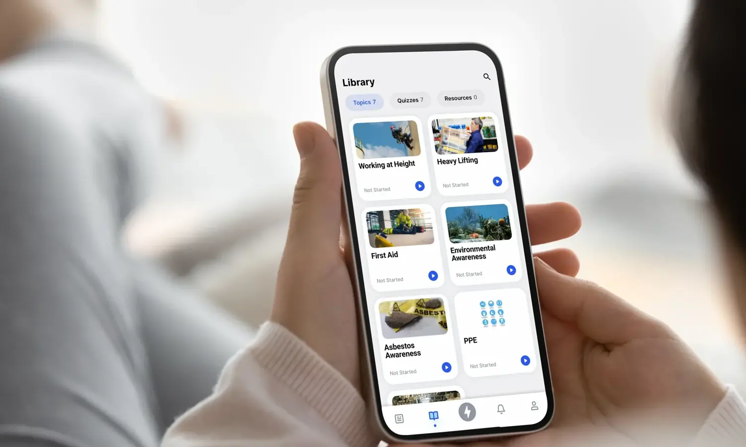 Pessoa que utiliza uma aplicação para smartphone para navegar numa biblioteca de cursos, incluindo "Trabalho em altura", "Primeiros socorros", "Sensibilização para o amianto", entre outros, com opções categorizadas em vários tópicos e sectores.