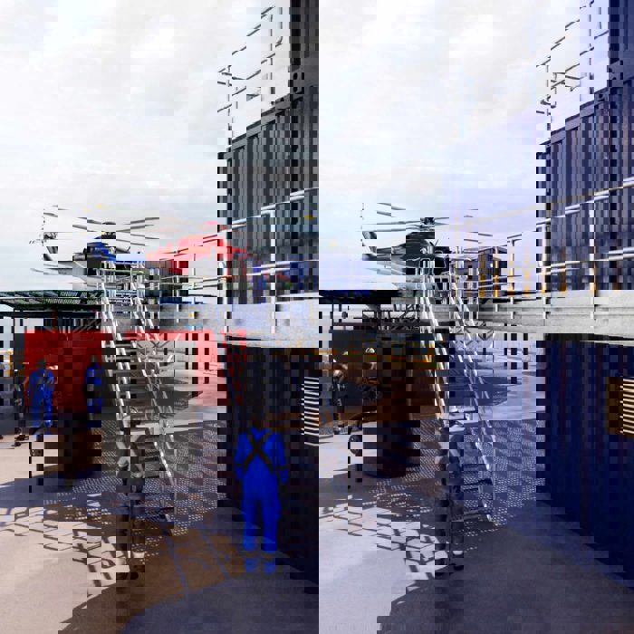 Helicóptero numa plataforma com trabalhadores de uniforme azul nas proximidades, situado ao lado de contentores de metal.