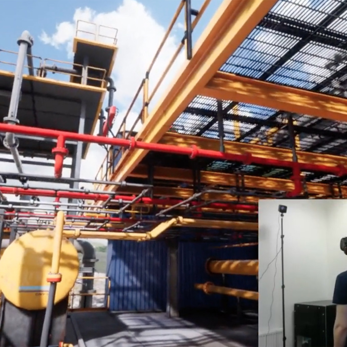 Uma pessoa com auscultadores de realidade virtual está imersa num ambiente industrial virtual que apresenta maquinaria, tanques amarelos e condutas vermelhas.