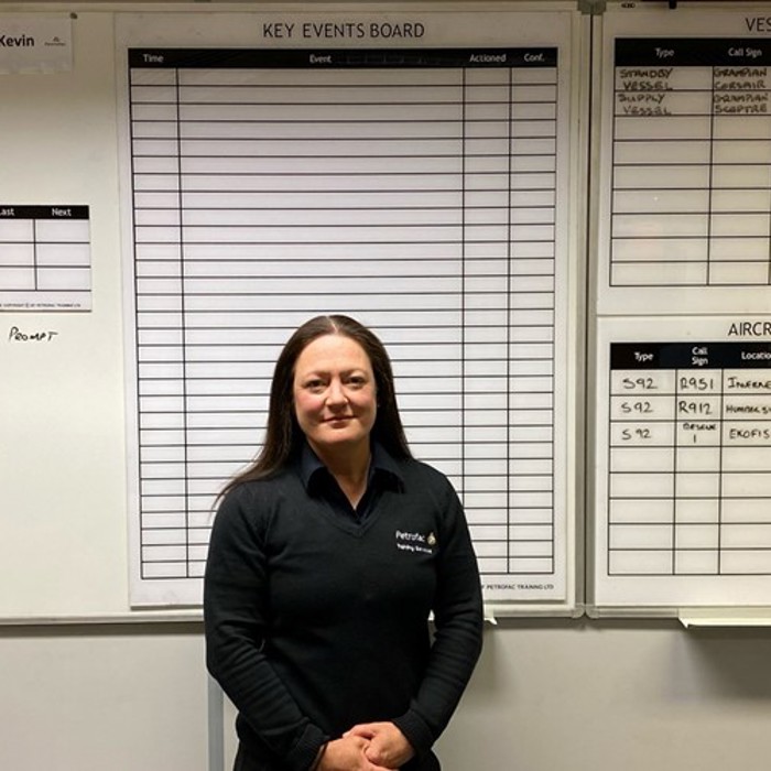 A person stands in front of a whiteboard with sections labeled "Key Events Board," "Vessel Availability," and "Aircraft Availability." The whiteboard has various rows and columns, mostly empty.