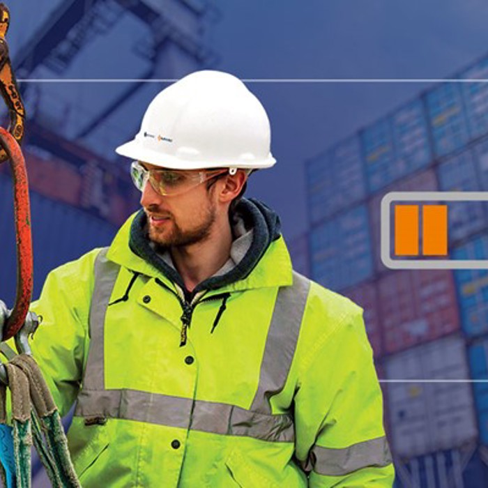 Two workers in high-visibility jackets and hard hats operate lifting equipment at a container yard, with an on-screen battery icon and a red recording indicator overlay.