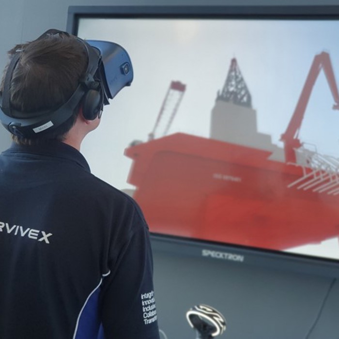 A person wearing a VR headset interacts with a virtual simulation of an offshore rig displayed on a large screen.