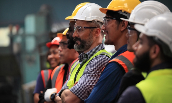 A group of workers wearing safety helmets and vests stands together, focusing intently on a training exercise just out of view.