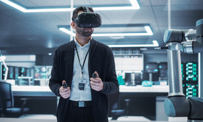A person wearing a virtual reality headset operates a robotic arm using handheld controllers in a modern, high-tech room.