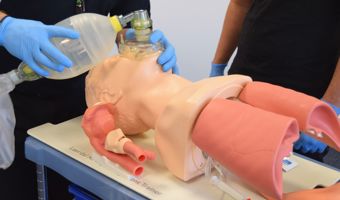 Two individuals practice CPR and ventilation techniques on a medical mannequin torso using a bag valve mask.
