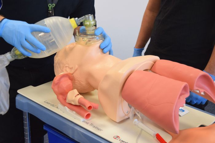 Two individuals practice CPR and ventilation techniques on a medical mannequin torso using a bag valve mask.