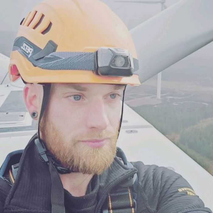 wind technician with orange helmet on the top of a wind turbine. In the background are the blades and countryside.