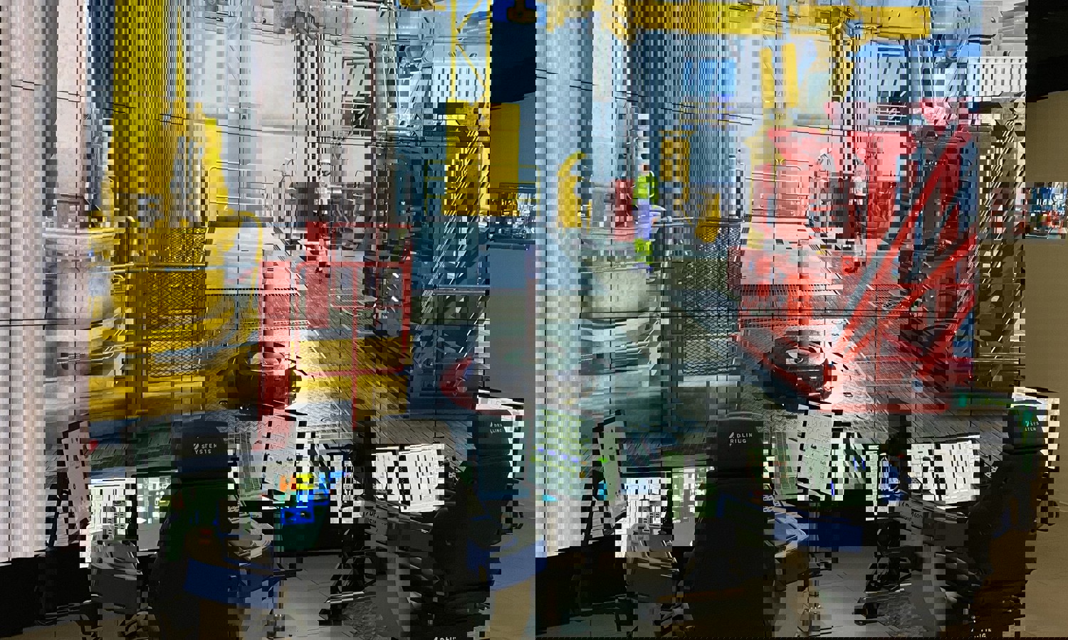 Control room setup with multiple screens and workstations displaying a detailed drilling rig simulation. Operators' chairs and monitors are in the foreground, while the virtual rig scene is in the background.