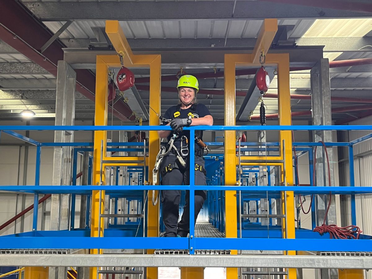3t instructor with a neon helmet standing on a blue and yellow working at height skills frame.