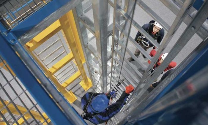 Workers wearing safety gear climb and stand on a metal industrial structure.