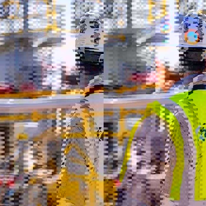 A worker wearing a high-visibility vest and a hard hat stands looking at an industrial site with various pipes and structures. The vest reads "KENTECH.