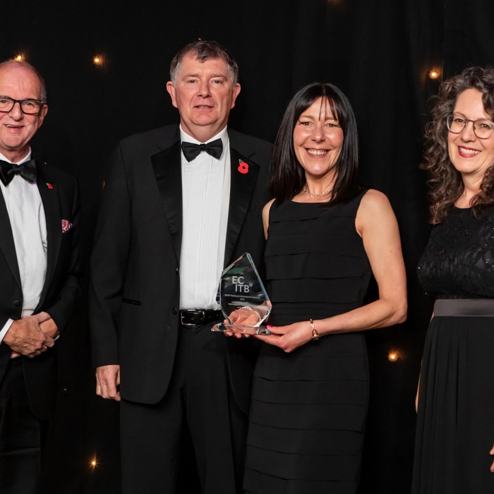 Four people in formal attire stand together against a black backdrop, showcasing their achievements after intensive training. The woman second from the right proudly holds a glass award as evidence of her success.