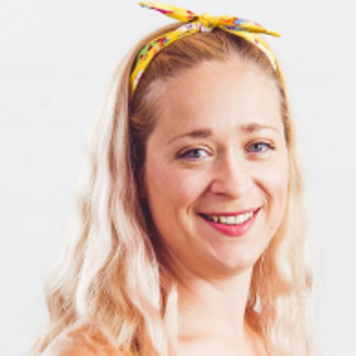 A woman with long blonde hair, wearing a yellow headband, smiles in front of a plain white background.