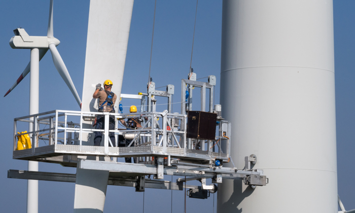 Workers on a platform engage in specialized training while performing maintenance on a large wind turbine.