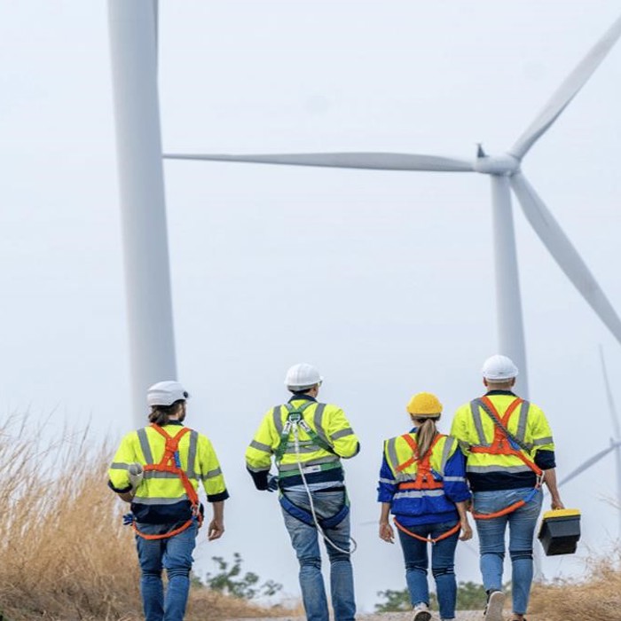 Four workers in safety gear, fresh from a training session, walk toward wind turbines in a field.